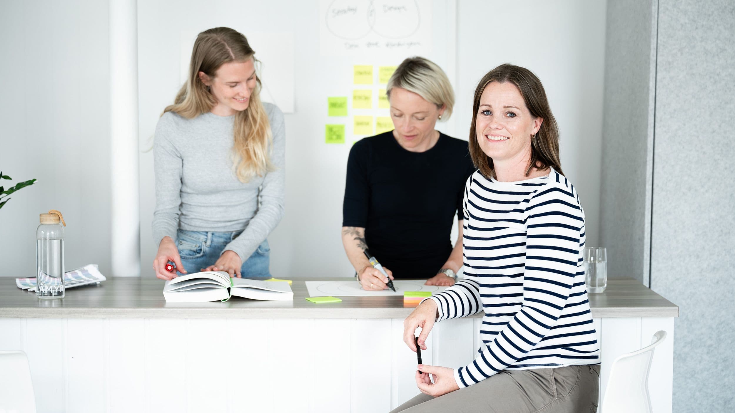 Johanna, Sunniva og Therese i arbeid ved en benk på kontoret.